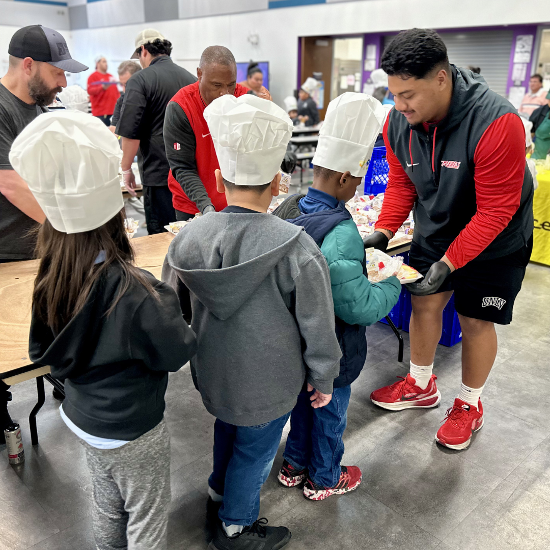 A UNLV Football player hands a plate of food to a kid
