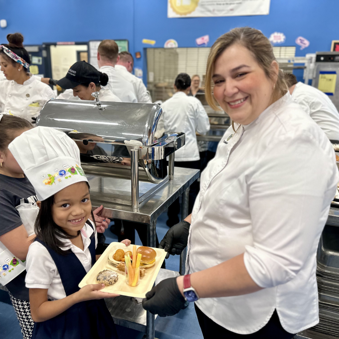 A female chef hands a plate of breakfast to a female student