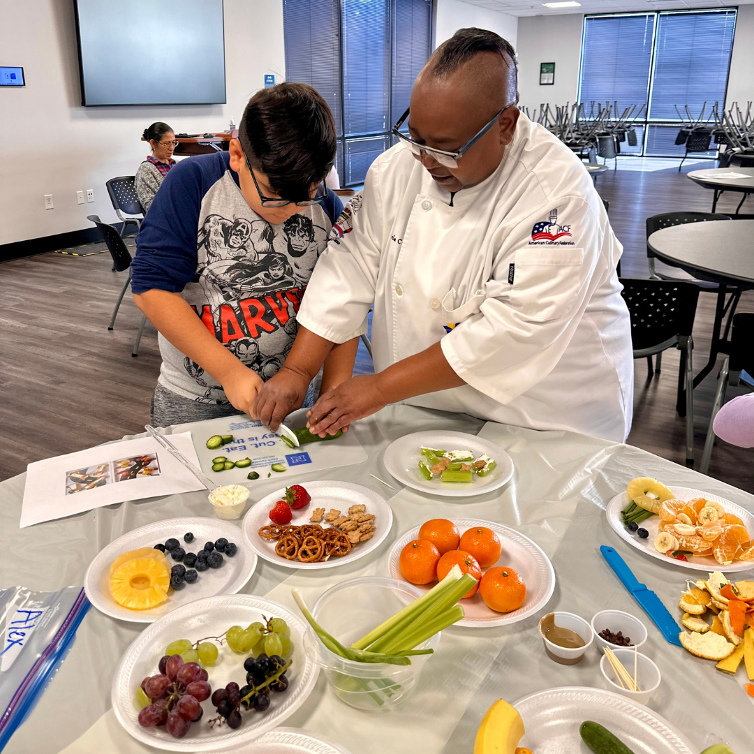A female chef volunteer teaches a young male student proper knife cutting skills