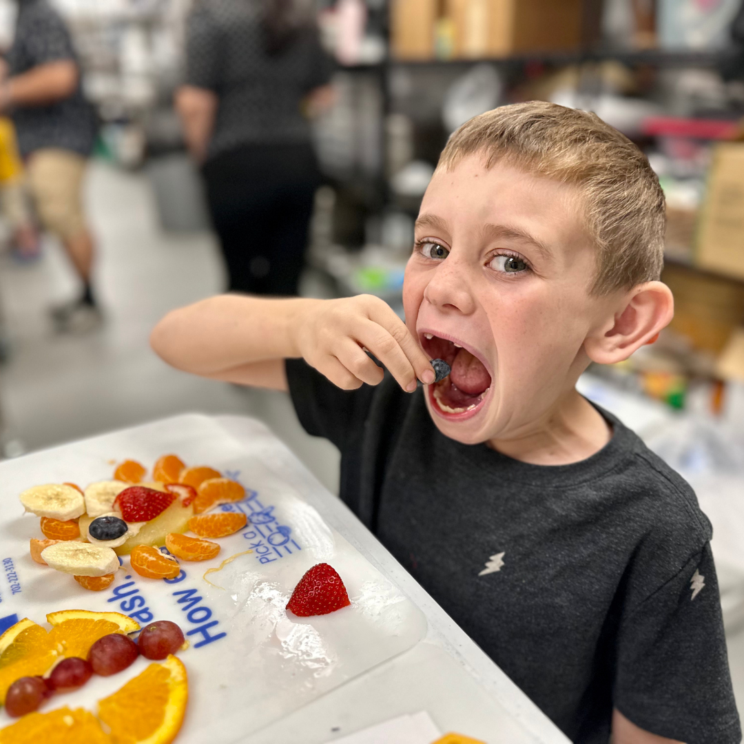 A kid eats a blueberry eye of a lion made out of produce