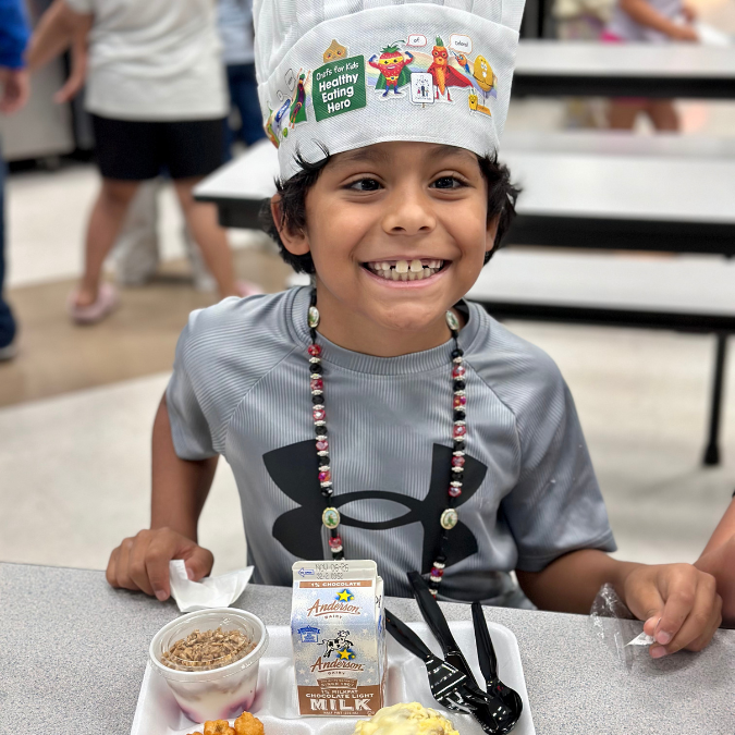A kid smiles over a plate of breakfast at Woolley ES