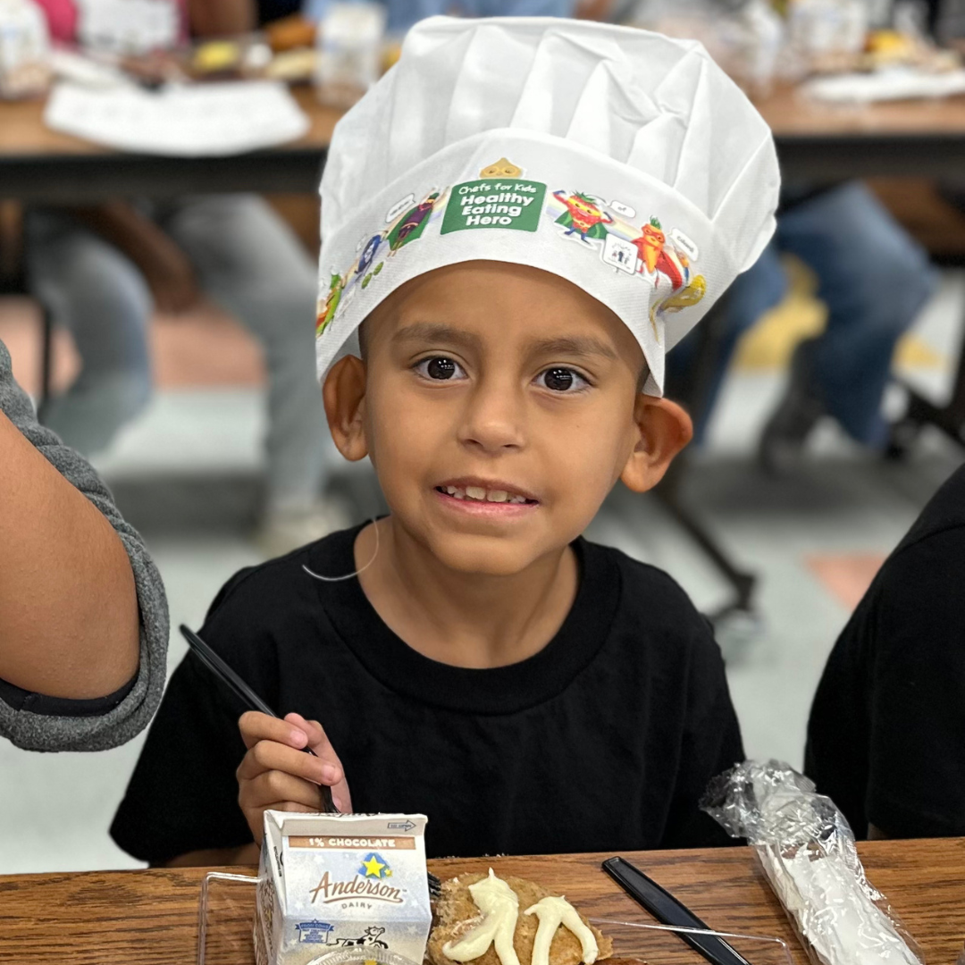 A male student in a chefs hat enjoys breakfast