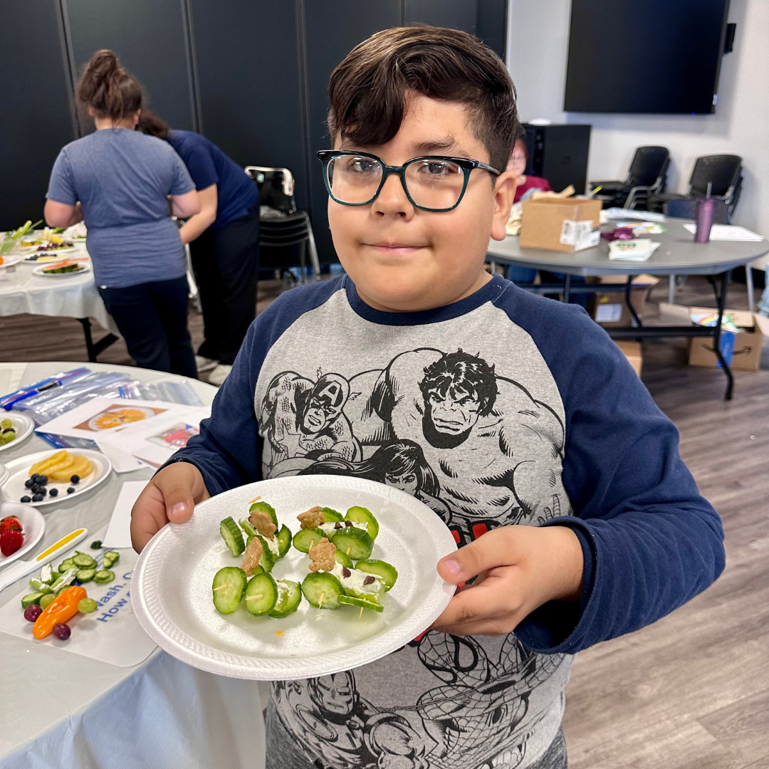 A male student shows off his teddy bear race cars made of produce