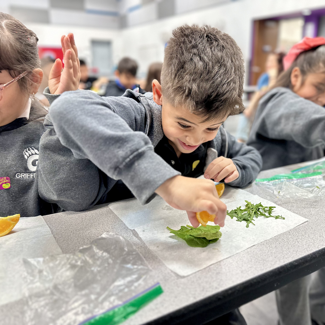 A male student squeezes an orange over some spinach