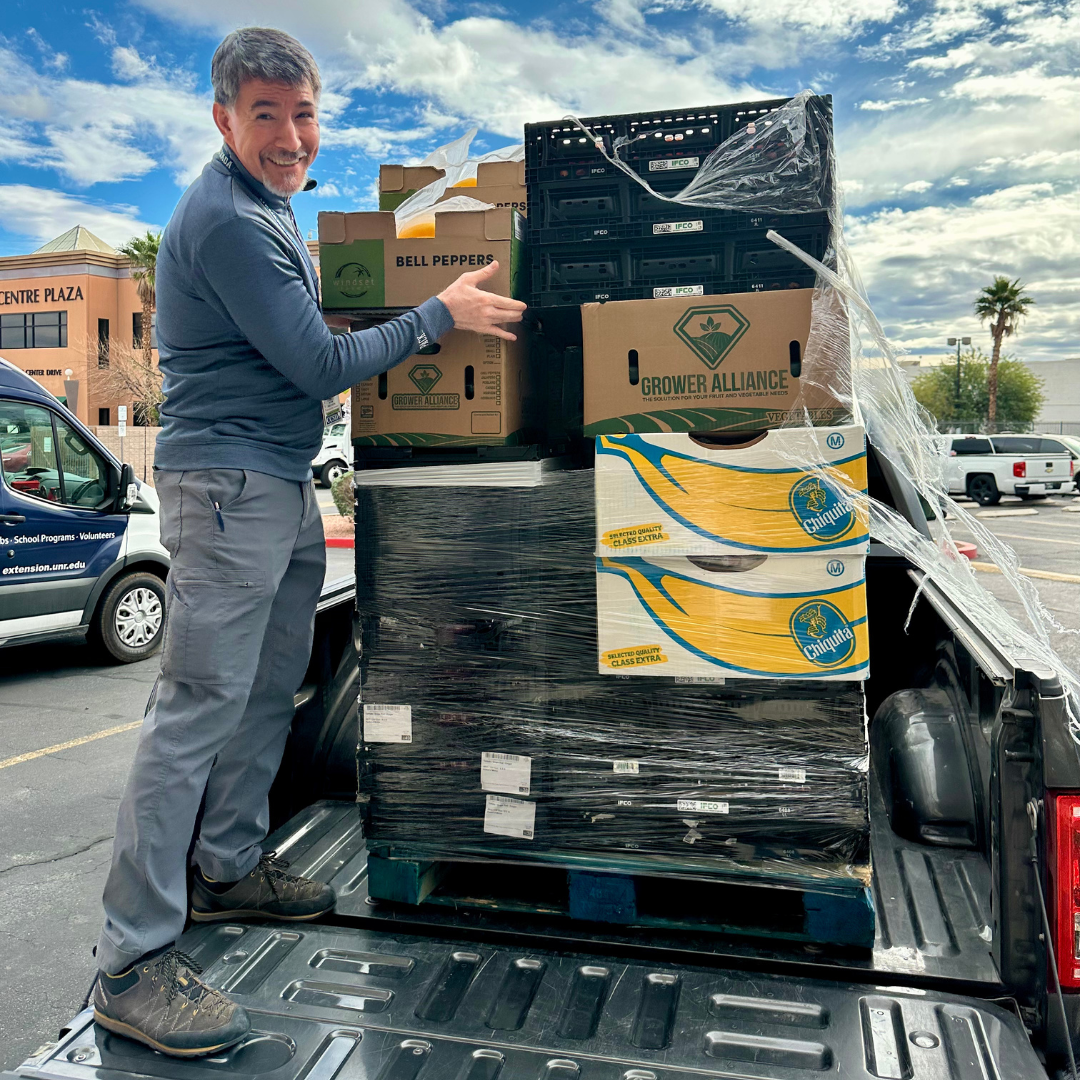 A man poses with a palette of fresh produce on top of a truck