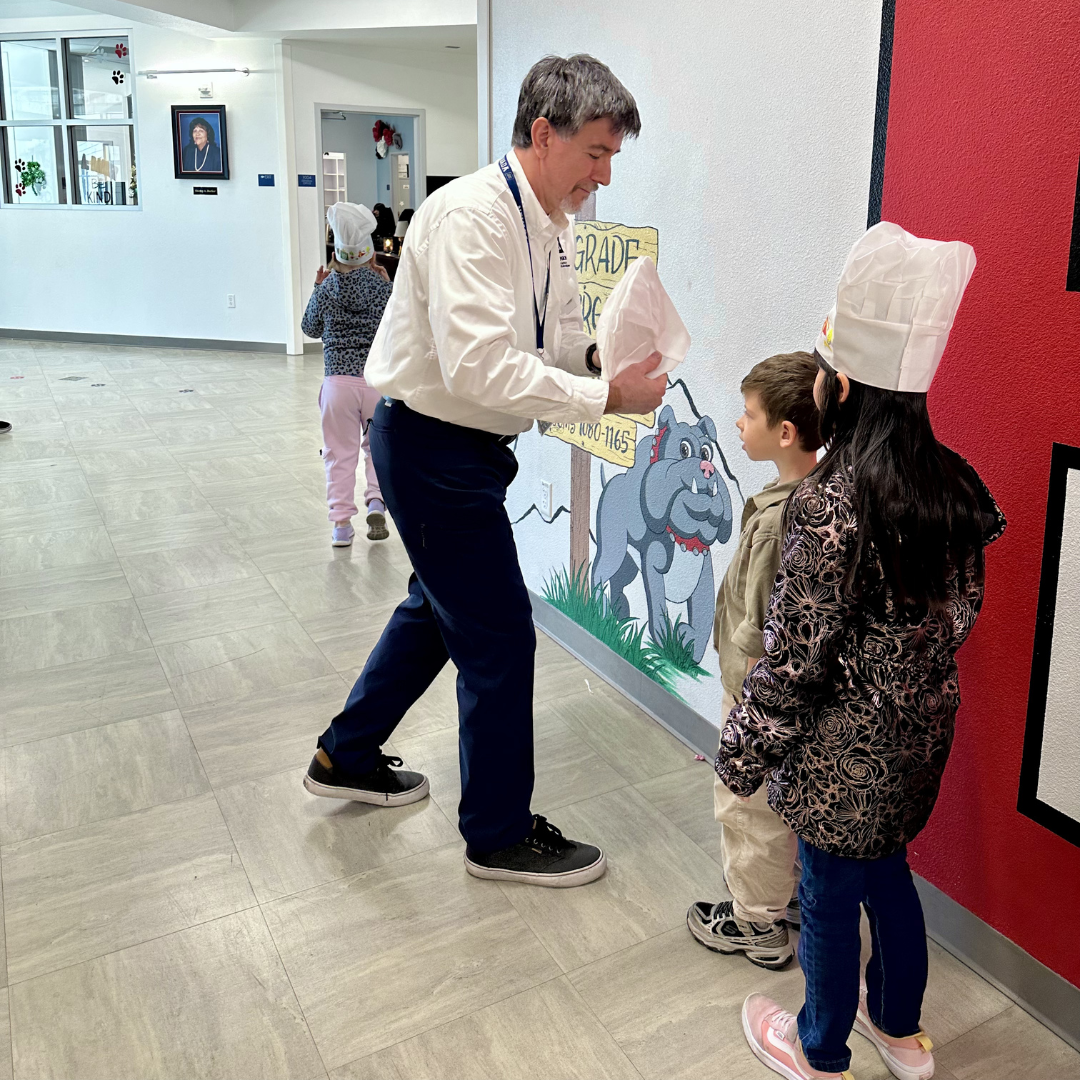 A man puts a chefs hat on a student