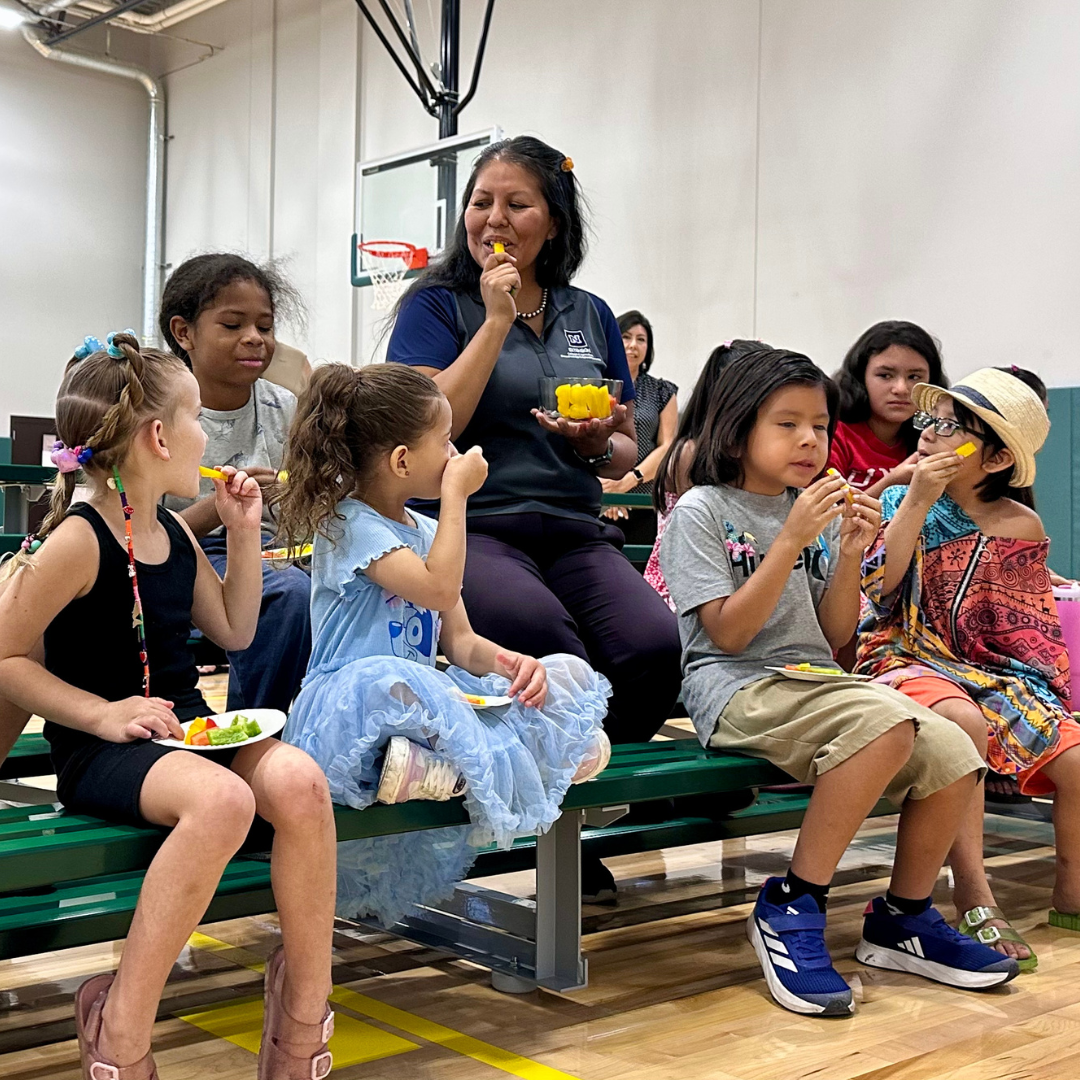 A teacher sits with kids as they try bell peppers