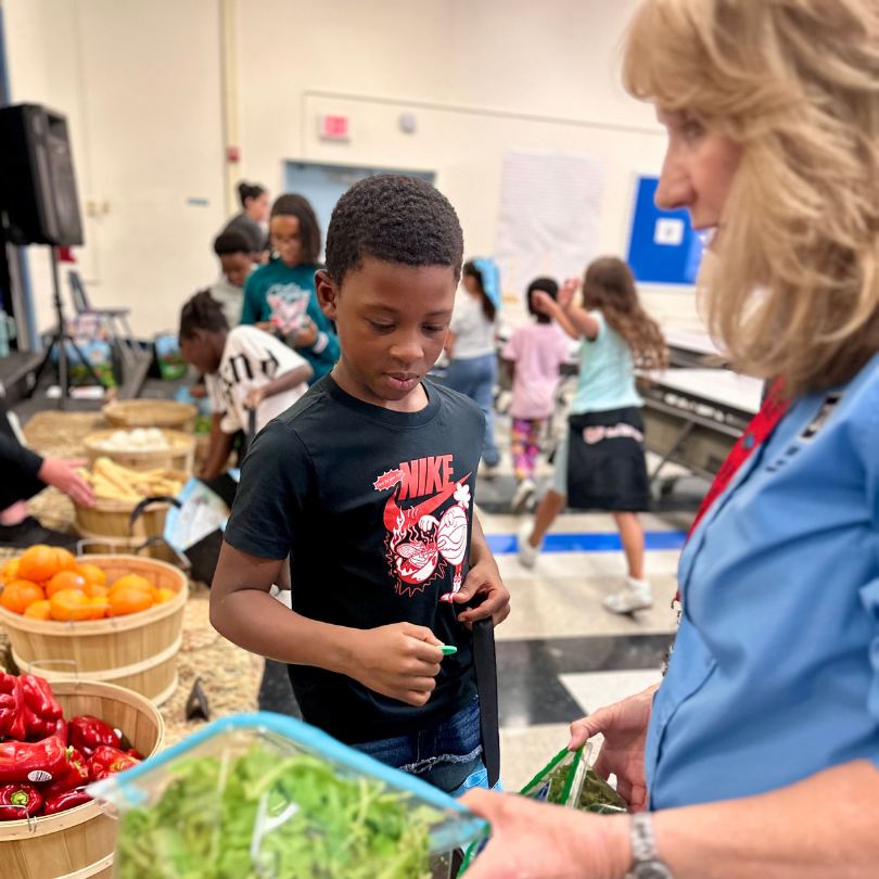 A woman holds spinach and arugula for a boy to choose from