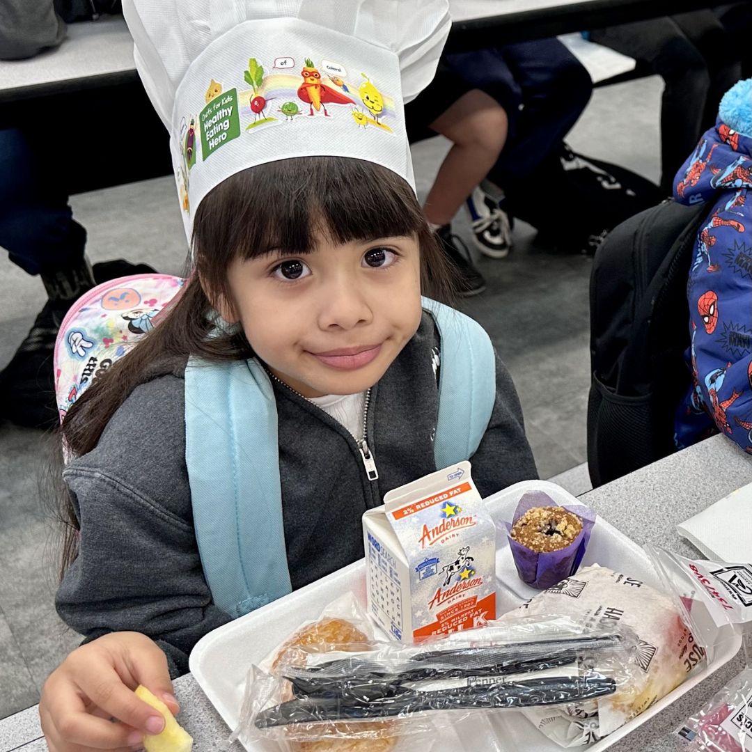A young girl in a chefs hat eats breakfast at Griffith ES