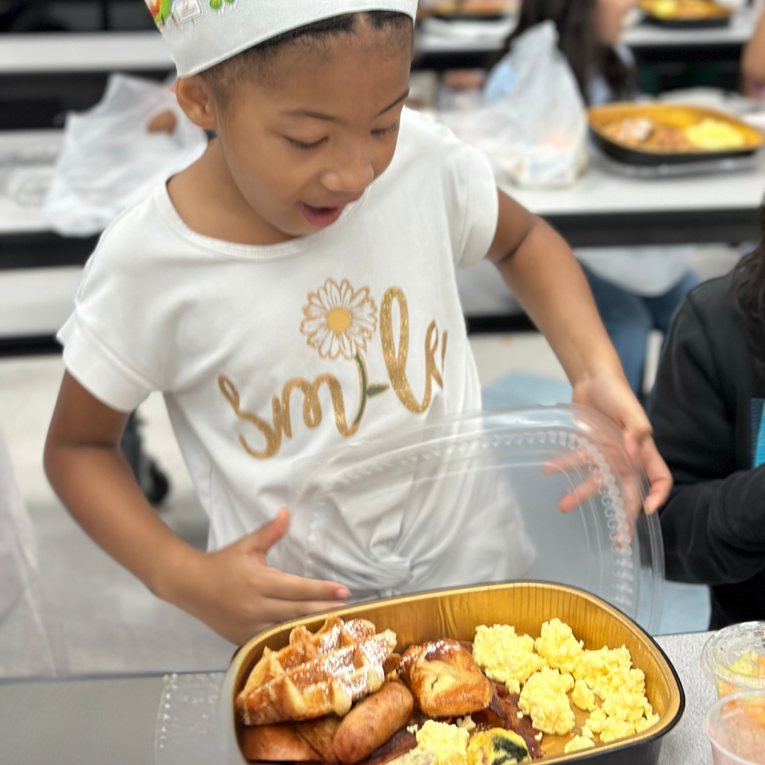 A young girl in a chefs hat smiles opening her breakfast