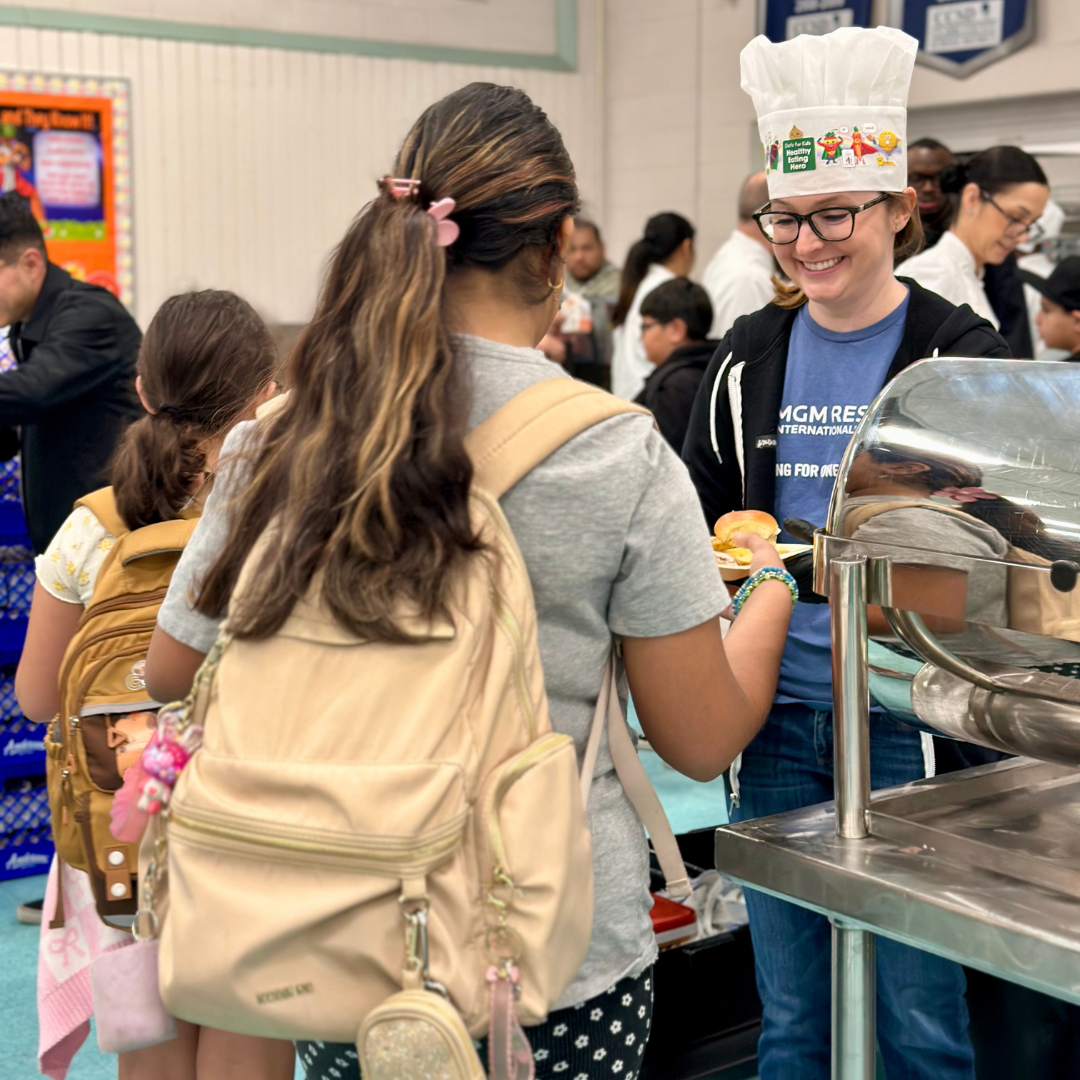 An MGM Volunteer hands a plate of food to a student