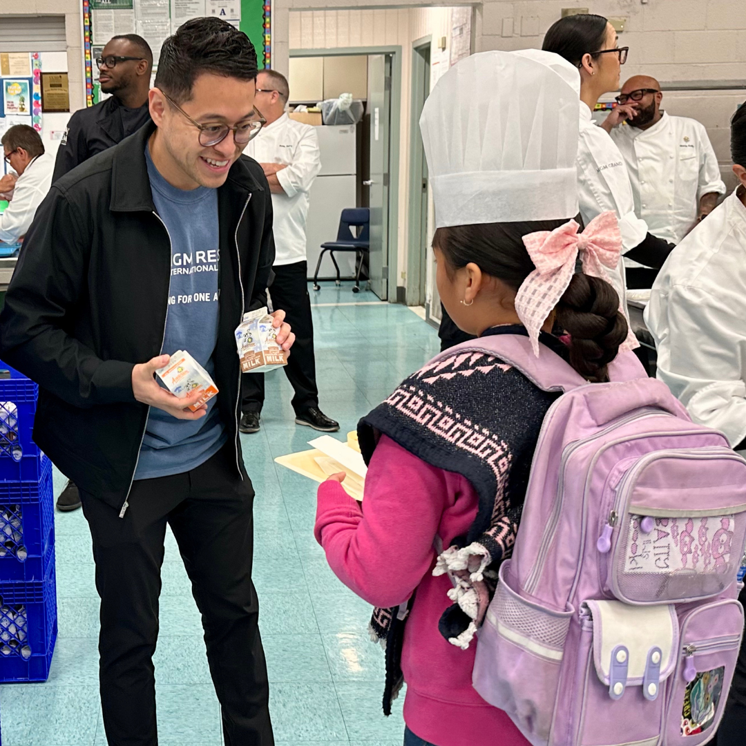 An MGM volunteer hands milk to a student
