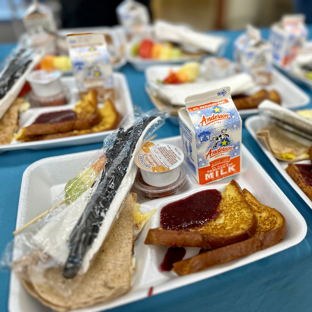 A tray of food including French toast with berry compote, a quesadilla, fruit kebab, milk, and plasticware.
