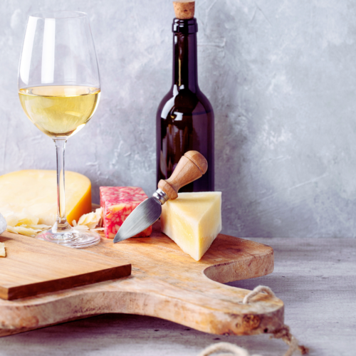 A glass and bottle of wine and some cheese sit on top of a board.