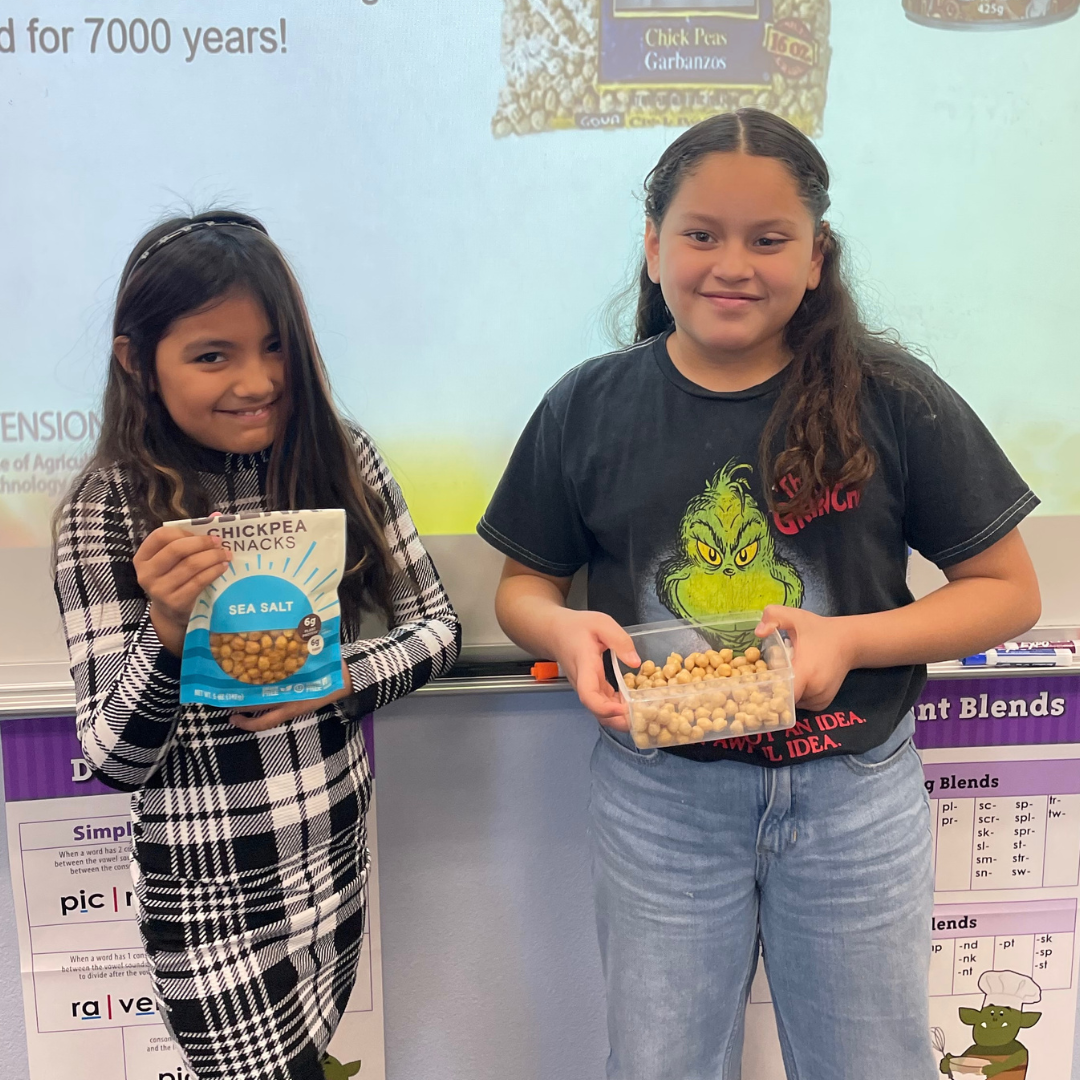 Two girls in a classroom holding containers of chickpeas.