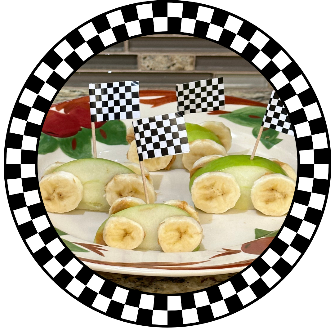 Sliced apples with sliced bananas made to look like little race cars with checkered flags sitting on a plate,