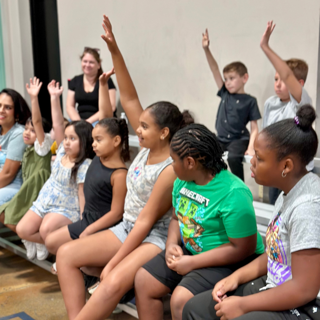 Several kids raise their hands in class