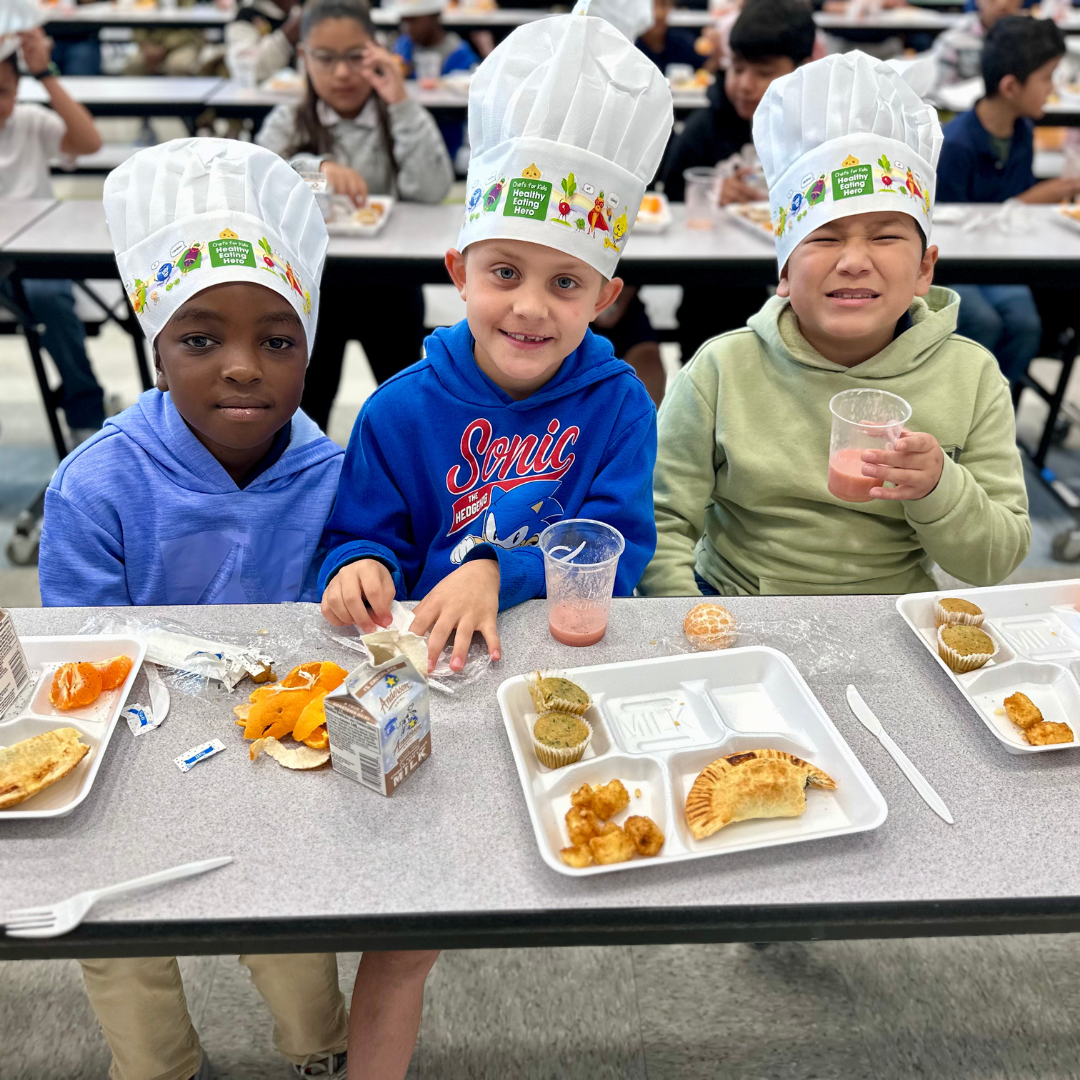 Three male students smile with breakfast in front of them