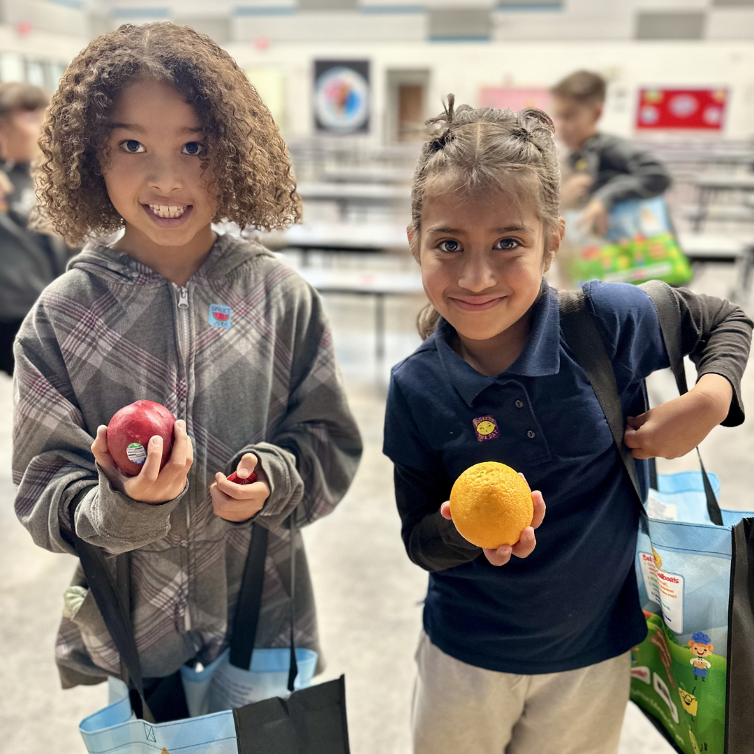 Two female students hold up produce at the farmers market