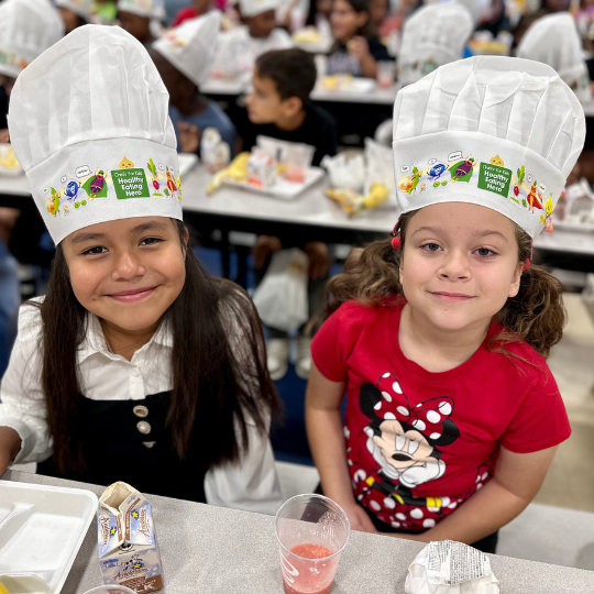 Two girls smiling for the camera wearing chefs hats