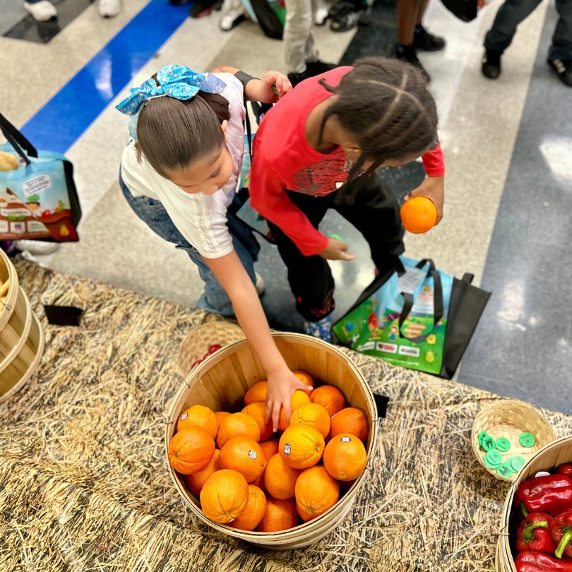 Two kids picking oranges out of a basket