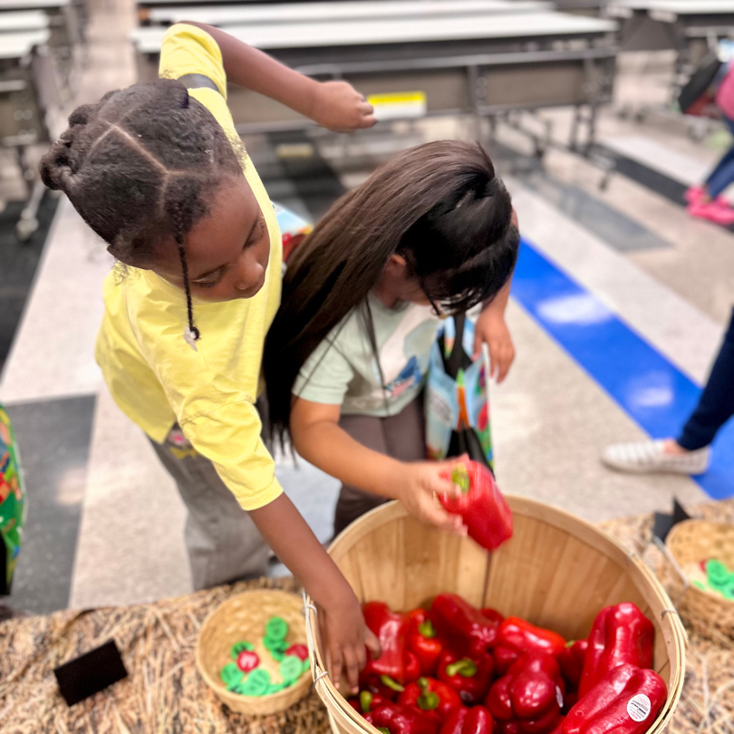 Two kids picking red bell peppers out of a basket